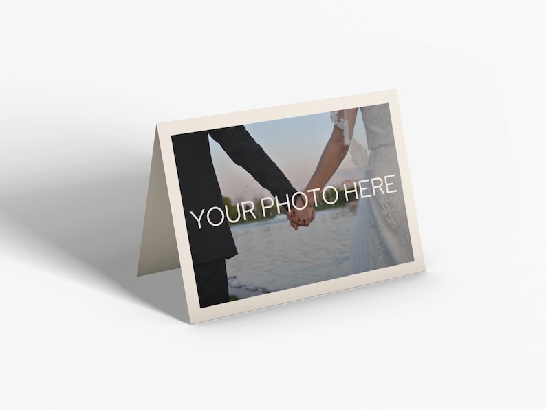 May include: A folded cream-colored card with a photograph of a couple holding hands. The photo has the text "YOUR PHOTO HERE" in white. The background of the photo shows a body of water and a blurred landscape.