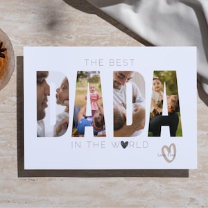 May include: A white card with the words "THE BEST DADA IN THE WORLD" cut out to reveal family photos. A glass of amber liquid with a star anise garnish sits to the left. A white cloth is draped in the background.