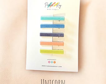 May include: Set of five velvet hair clips in various colors, including teal, blue, gray, peach, and yellow. The clips are arranged vertically on a white card with the text "Parker & Kay Boutique" and "www.parkerandkay.com". The word "UNICORN" is printed below the card.