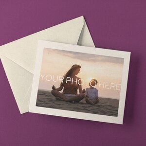 May include: A cream-colored envelope and a greeting card with a photograph of a person and child meditating on a beach at sunset. The card has a white border and the text "YOUR PHOTO HERE". The background is a solid purple.