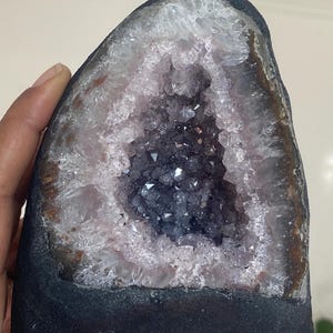 Peut inclure: Une grande géode d'améthyste avec un amas de cristaux violets foncés à l'intérieur. La géode est de formation naturelle et a un extérieur brun rugueux.