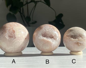 May include: Three pink and white agate crystal spheres on stands. The spheres are polished and have a natural, druzy finish. The spheres are labeled A, B, and C.