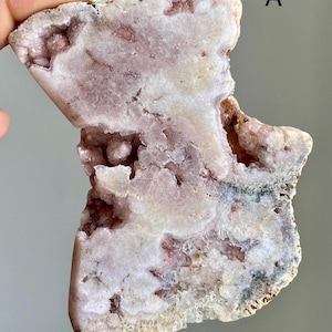 May include: A close-up of a natural, irregularly shaped stone with a mix of pink, white, and brown hues. The stone has a crystalline structure with visible cavities and the letter "A" in the upper right corner.