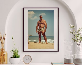 May include: A framed photograph of a muscular man standing on a beach. He is wearing khaki swim trunks and has a beard. The beach is sandy with blue water and white waves in the background.