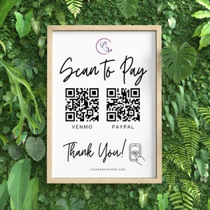May include: A framed sign with the text "Scan to Pay" and two QR codes for Venmo and PayPal. The sign also includes the words "Thank You!" and a website address. The background is a wall of green plants.