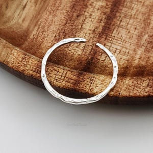 May include: A silver ring with a hammered texture. The ring is open and has a simple design.