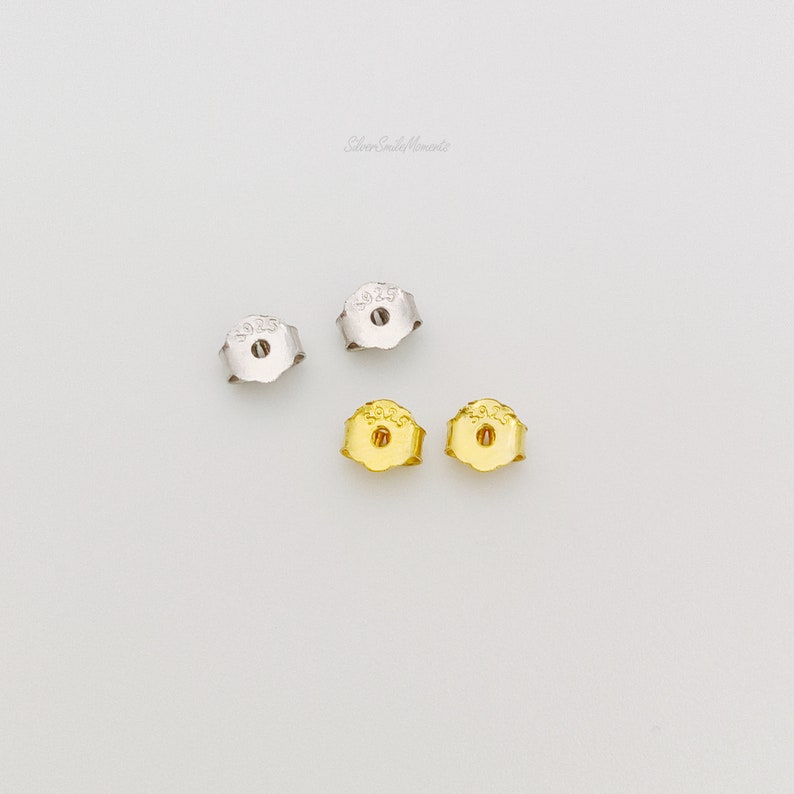 May include: Four earring backs, two silver and two gold. The silver backs are marked "925" and the gold backs are marked "925".