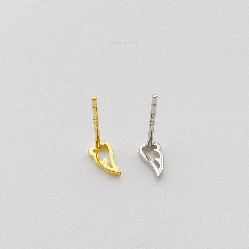 May include: Two pairs of earrings, one gold and one silver, in the shape of a wing. Both earrings have a post back.