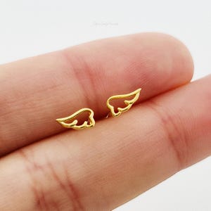 May include: A pair of gold-toned angel wing earrings. The wings are delicate and have a simple design.