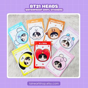 May include: A collection of seven waterproof vinyl stickers featuring cartoon characters wearing animal-themed hoods. Each sticker displays a unique character face and name, including RM x KOYA, JIN x RJ, SUGA x SHOOKY, J-HOPE x MANG, JIMIN x CHIMMY, V x TATA, and JK x COOKY on colorful rectangular backing cards.