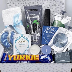 Pu&ograve; includere: Una scatola regalo contenente un asciugamano bianco con un nastro blu, una maschera in gel al carbone Freeman, un pettine nero, due bustine di t&egrave; Pukka, due bustine in alluminio, due piccole candele rotonde, una barretta di cioccolato Yorkie e un sapone grigio.