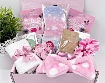 Può includere: Una confezione regalo rosa piena di articoli per la cura di sé. Include una mascherina per dormire, maschere per il viso, una fascia per capelli, un asciugamano con un fiocco rosa e un braccialetto con la scritta "Make a Wish". La scatola è decorata con articoli rosa e bianchi.
