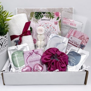 May include: A pink and white gift box filled with beauty products. The box contains a pink face mask, a pink clay mask, a white sheet mask, a white towel, a pink headband, a white bottle of face serum, a white bottle of body lotion, and a pink and white box of face masks.