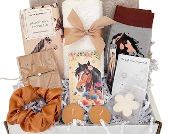 Può includere: Una confezione regalo contenente una tavoletta di cioccolato Galaxy Milk, un asciugamano bianco con nastro beige, calzini grigi con stampa di cavalli, un braccialetto Make a Wish, un taccuino con cavalli, una penna, orecchini a ferro di cavallo, un elastico color ruggine e due candele.