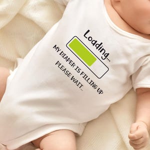 May include: White baby onesie with a black and green graphic that says "Loading... My diaper is filling up. Please wait..." with a green progress bar.