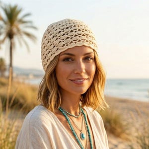 Könnte beinhalten: Eine cremefarbene Häkelmütze mit einem sich wiederholenden Muschelmuster. Die Mütze ist aus feinem Garn gefertigt und weist eine zarte, durchbrochene Textur auf, die den Kopf bedeckt und eine leichte sowie atmungsaktive Passform bietet.