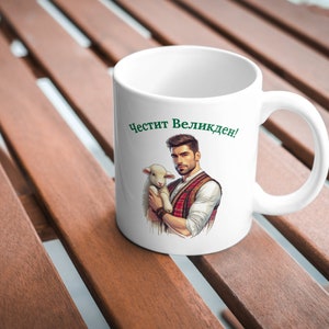 Pu&ograve; includere: Tazza in ceramica bianca con un'illustrazione verde e rossa di un uomo che tiene un agnello. Il testo "Честит Великден!" &egrave; stampato sulla tazza.