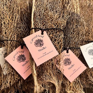 May include: Dried, fibrous cholla cactus wood segments with a natural tan, porous texture. Each piece is tied with black string to a square, light pink tag featuring the text Carved Soul Studio and a floral illustration with an email address.