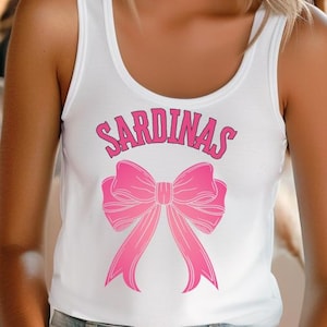 May include: White tank top with a pink bow and the text "SARDINAS" printed on the front.