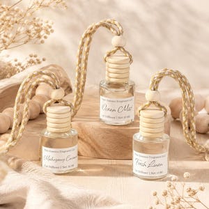 Pode incluir: Três frascos difusores de carro em vidro transparente com tampas de madeira e cordões trançados para pendurar. Cada frasco possui um rótulo branco com o texto Pure Essence Fragrance LLC, o nome do aroma e Net 10 ml.