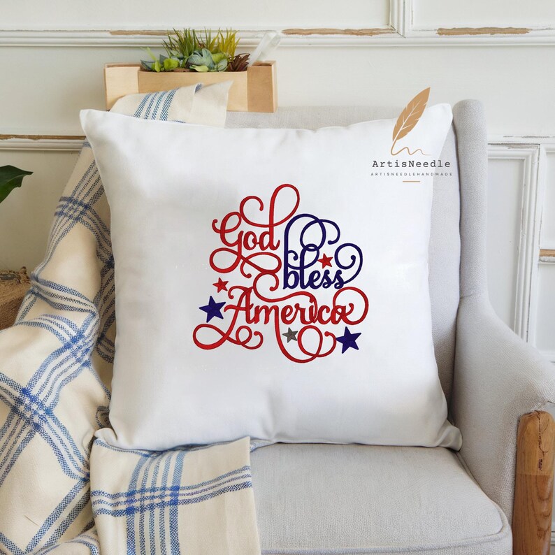 May include: A white square throw pillow featuring the red and blue embroidered text God bless America in a decorative script font. The design is accented with small red, blue, and silver stars scattered around the lettering on the front surface.