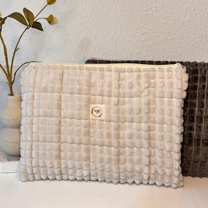 Könnte beinhalten: Zwei Reißverschlusstaschen, eine beige und eine dunkelbraun, mit einer gesteppten Textur. Die beige Tasche hat ein kleines weißes Etikett mit dem Text "NRB" in Schwarz.