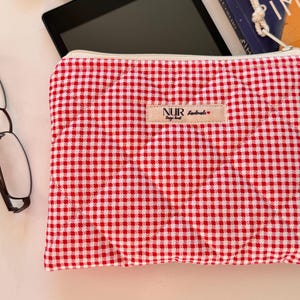 Op de afbeelding: Rode en witte gingham rits-tas met een wit label waarop "NUR Design Hand" en een klein rood hartje staat.