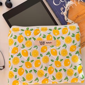 Könnte beinhalten: Eine weiße, gesteppte Reißverschlusstasche mit Zitronenmuster. Die Tasche hat ein Etikett mit der Aufschrift "NUR Handmade" und einem kleinen roten Herz.