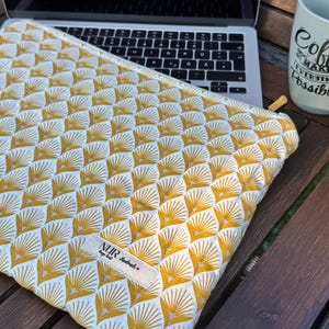 Op de afbeelding: Een gele en witte laptophuls met een geometrisch patroon. De hoes heeft een klein label met de tekst "NUR design handmade".