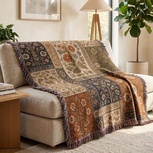 Könnte beinhalten: Eine gewebte Wohndecke mit einem Patchwork-Design aus Blumenmustern in Rost, Marineblau, Creme und Salbeigrün. Die rechteckige Decke hat einen Fransenrand und liegt über einem hellen Sofa in einem hellen Wohnbereich.