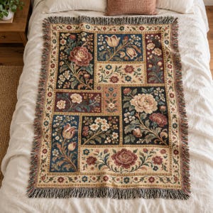 May include: A rectangular woven throw blanket featuring a patchwork design of floral motifs in shades of burgundy, cream, blue, and green. The blanket has a decorative border and fringed edges on all four sides, displaying intricate botanical patterns.