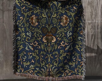 May include: A woven tapestry throw blanket with a blue background and a repeating pattern of stylized flowers and leaves in shades of green, brown, and cream. The blanket has a fringe border.