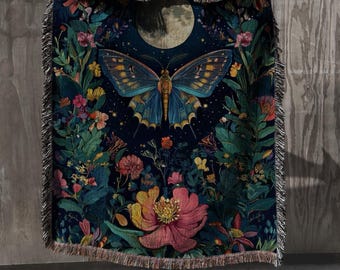 Könnte beinhalten: Eine dunkelblaue gewebte Tagesdecke mit einem großen Schmetterling mit blau-goldenen Flügeln, umgeben von bunten Blumen und Blättern. Im Hintergrund ist ein Vollmond zu sehen. Die Decke hat einen Fransenrand.