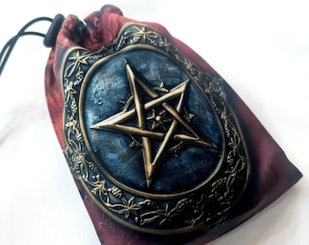 May include: A burgundy and blue drawstring bag featuring a gold pentagram design. The bag has a detailed, ornate border around the pentagram. The bag is made of a soft material and has a black drawstring closure.