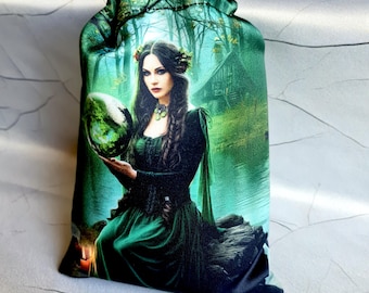 May include: A drawstring bag featuring a woman in a green dress holding a green orb. The background depicts a forest scene with a cabin. The bag is primarily green with a satin-like sheen.