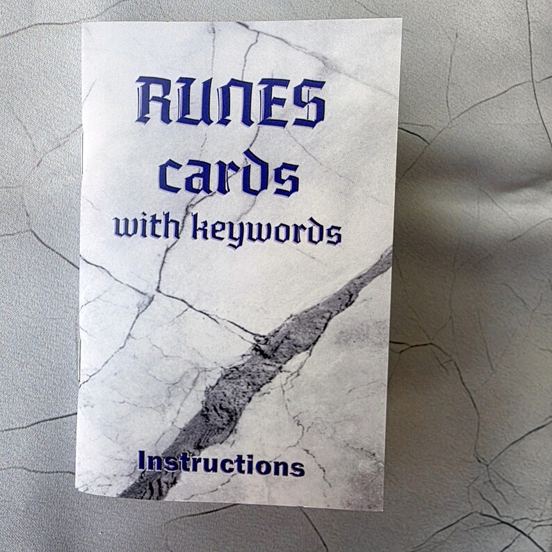 May include: A folded card with a marble-like pattern and the words "RUNES cards with keywords" in blue. The word "Instructions" is printed at the bottom. The card is white with gray veining.