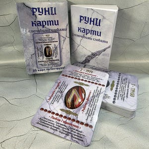 May include: A set of rune cards with accompanying booklets. The cards and boxes feature text in a foreign language, with a marble-like background. The cards display symbols and text, with a focus on health, love, and finances.