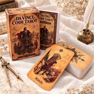 Pode incluir: Um baralho de tarot Da Vinci Code com caixa, livreto de instruções e cartas com ilustrações em tom sépia. A caixa exibe o título e uma figura num carro mecânico. Uma carta 10 de Paus é visível, ao lado de um compasso de metal.