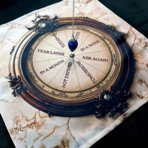 May include: A circular divination board with a pendulum. The board has eight sections with the following text: "Year Later", "In a Month", "Not Defined", "Tomorrow", "Today", "Later", "In a Week", and "Ask Again".