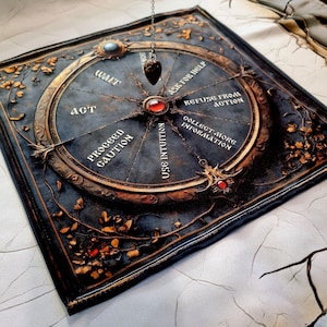 Puede incluir: Un tablero de adivinación circular con un péndulo colgando sobre él. El tablero tiene un fondo azul oscuro con detalles dorados y presenta las palabras "ACT", "WAIT", "PROCEED WITH CAUTION", "USE INTUITION", "ASK FOR HELP", "REFUSE FROM ACTION" y "COLLECT MORE INFORMATION".