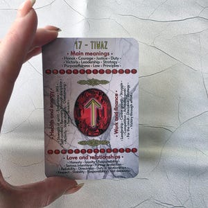 May include: A rectangular card with the text "17 - TIWAZ" and various keywords related to health, energy, work, finance, love, and relationships. The card features a central red gem with a gold arrow symbol.