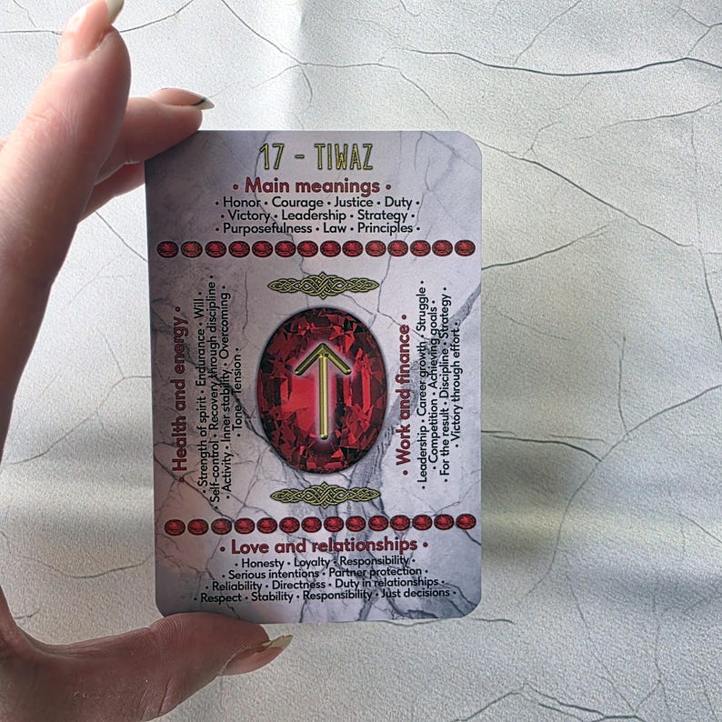 May include: A rectangular card with the text "17 - TIWAZ" and various keywords related to health, energy, work, finance, love, and relationships. The card features a central red gem with a gold arrow symbol.