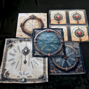 Puede incluir: Conjunto de cinco herramientas de adivinación de estilo vintage, que incluyen una planchette, una tabla ouija, una rueda de la fortuna y dos ruedas de adivinación. Las herramientas están impresas en tela y presentan marcos dorados ornamentados y diseños intrincados.