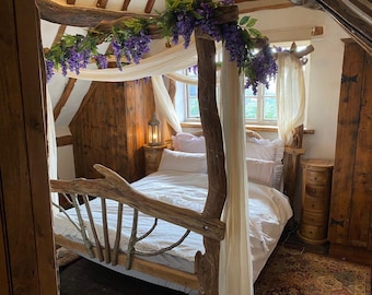 Puede incluir: Un dormitorio rústico con una cama con dosel. La estructura de la cama es de madera natural, y el dosel está cubierto con tela blanca y adornado con flores moradas. La habitación cuenta con muebles de madera y un ambiente suave y acogedor.