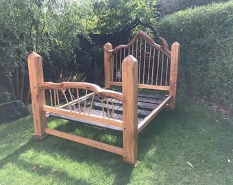 Puede incluir: Un marco de cama de madera hecho a mano con un diseño rústico natural. El cabecero y el piecero presentan listones verticales y detalles de madera curvada. El marco de la cama es de madera marrón claro y está sobre un césped.