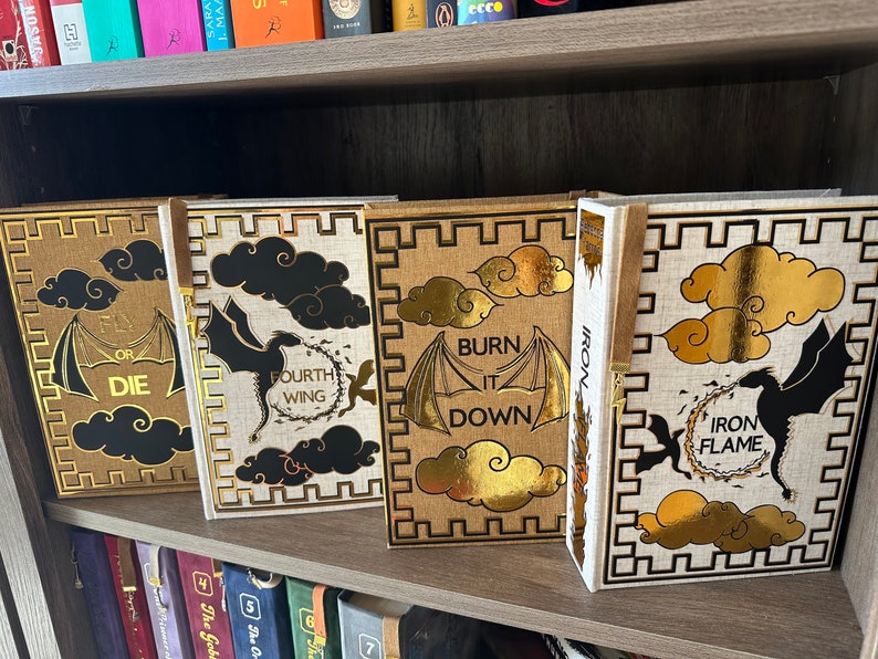 Pode incluir: Quatro livros de capa dura com desenhos dourados e pretos sobre um fundo branco. Os livros s&atilde;o intitulados "Fly or Die", "Fourth Wing", "Burn It Down" e "Iron Flame".