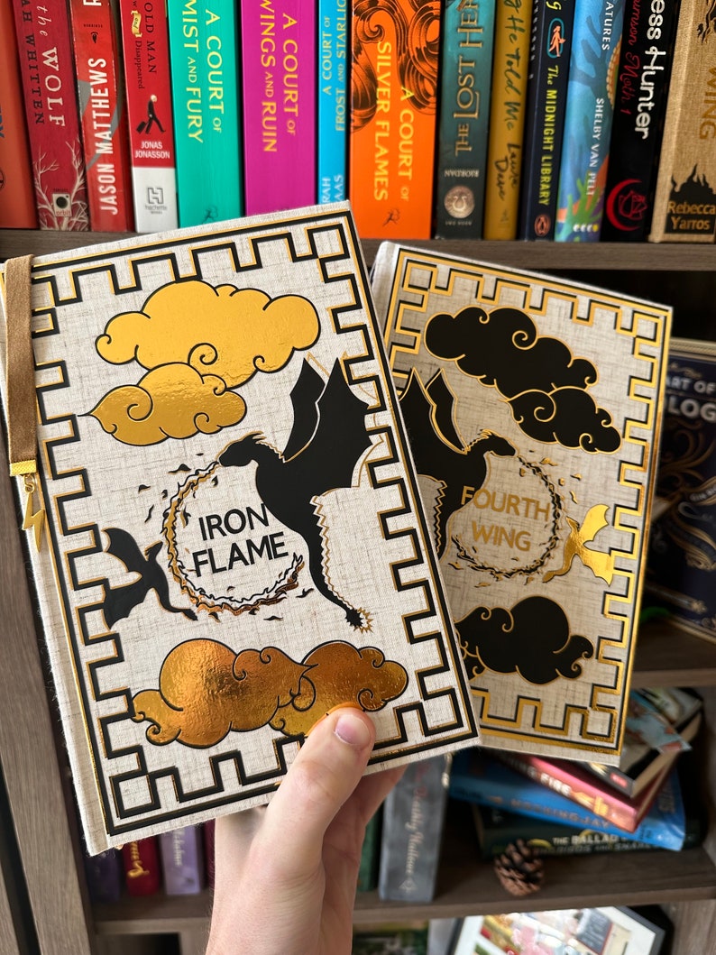 Pode incluir: Dois livros de capa dura com desenhos de drag&otilde;es dourados e pretos. O livro &agrave; esquerda tem o t&iacute;tulo "Iron Flame" e o livro &agrave; direita tem o t&iacute;tulo "Fourth Wing".