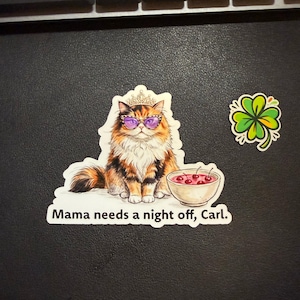 May include: A sticker featuring a long-haired calico cat wearing a gold crown and purple-tinted cat-eye glasses, sitting next to a bowl of red cherries. The text below the cat reads, Mama needs a night off, Carl. A separate four-leaf clover sticker.