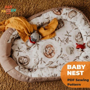 Könnte beinhalten: Ein Babynest mit floralem Muster und einem hellrosa Waffelrand. Das Nest enthält eine gelbe Decke, ein graues Stofftier und ein rotes pilzförmiges Spielzeug. Der Text "BABY NEST PDF Sewing Pattern" ist sichtbar.