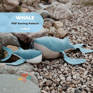 Può includere: Due giocattoli a forma di balena, blu e beige, appoggiati su rocce. Le balene hanno pinne dettagliate e cuciture. Il testo sull'immagine recita "WHALE PDF Sewing Pattern" e "4 sizes".